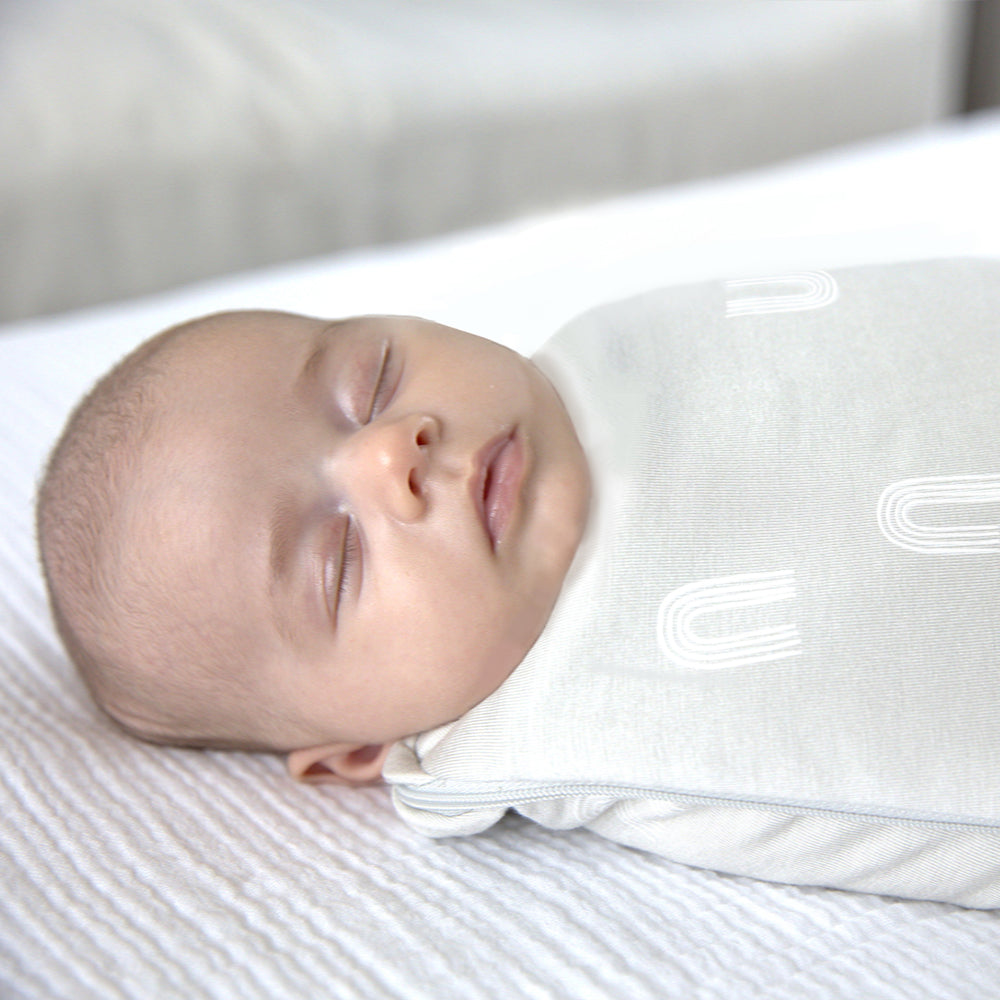 sleeping newborn baby in neutral colored rainbow printed swaddle