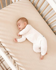 baby smiling in their sleep in a wooden crib on a beige crib sheet wearing undyed hypoallergenic baby pajamas for sensitive skin