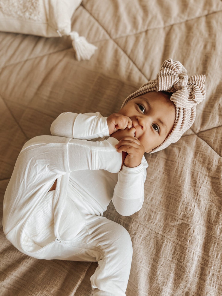 baby girl on a dark beige sheet wearing undyed hypoallergenic baby pajamas for sensitive skin