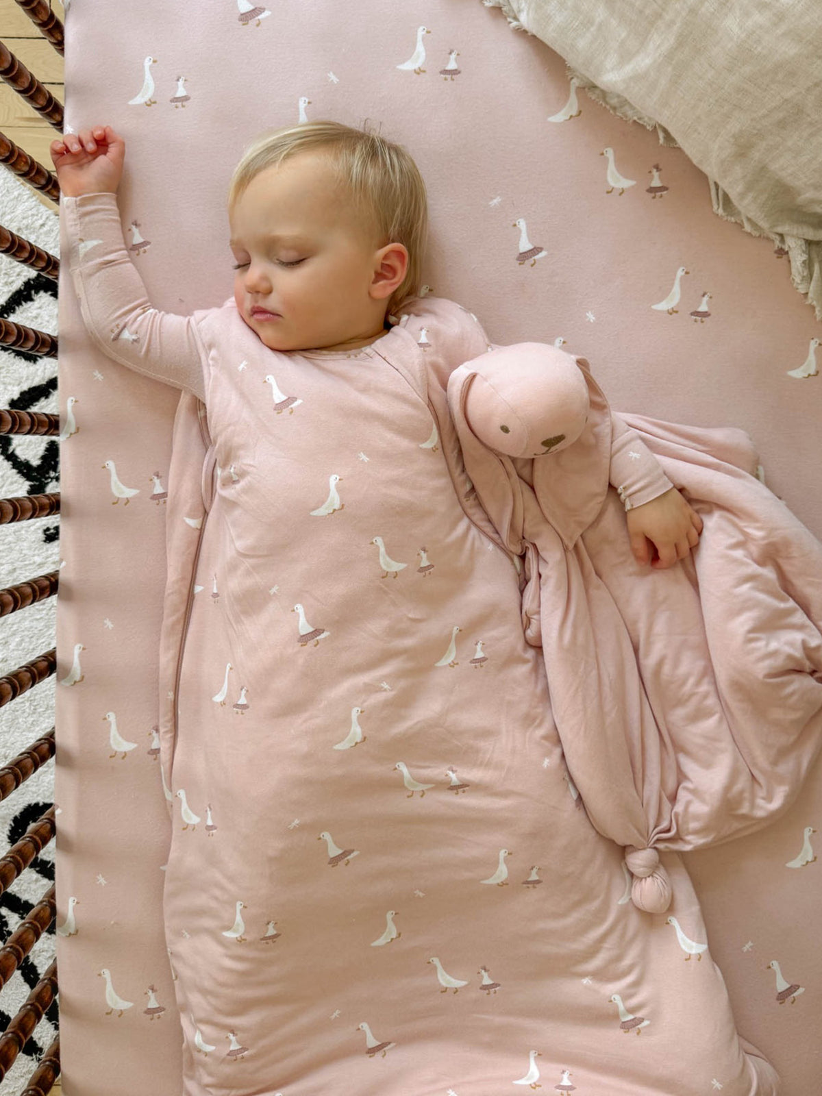 Pink crib sheet with repeating white goose pattern, baby lying on it