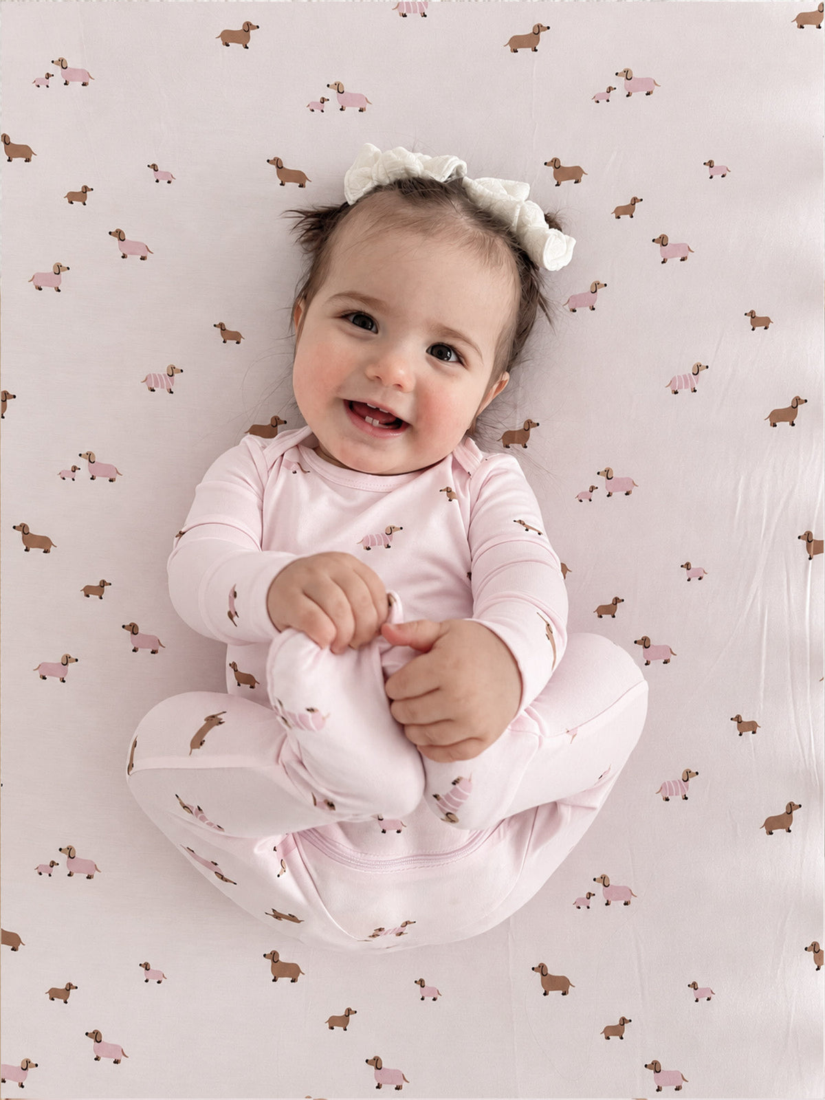 Light pink dog-print footed pajama, long sleeves; baby wearing headband