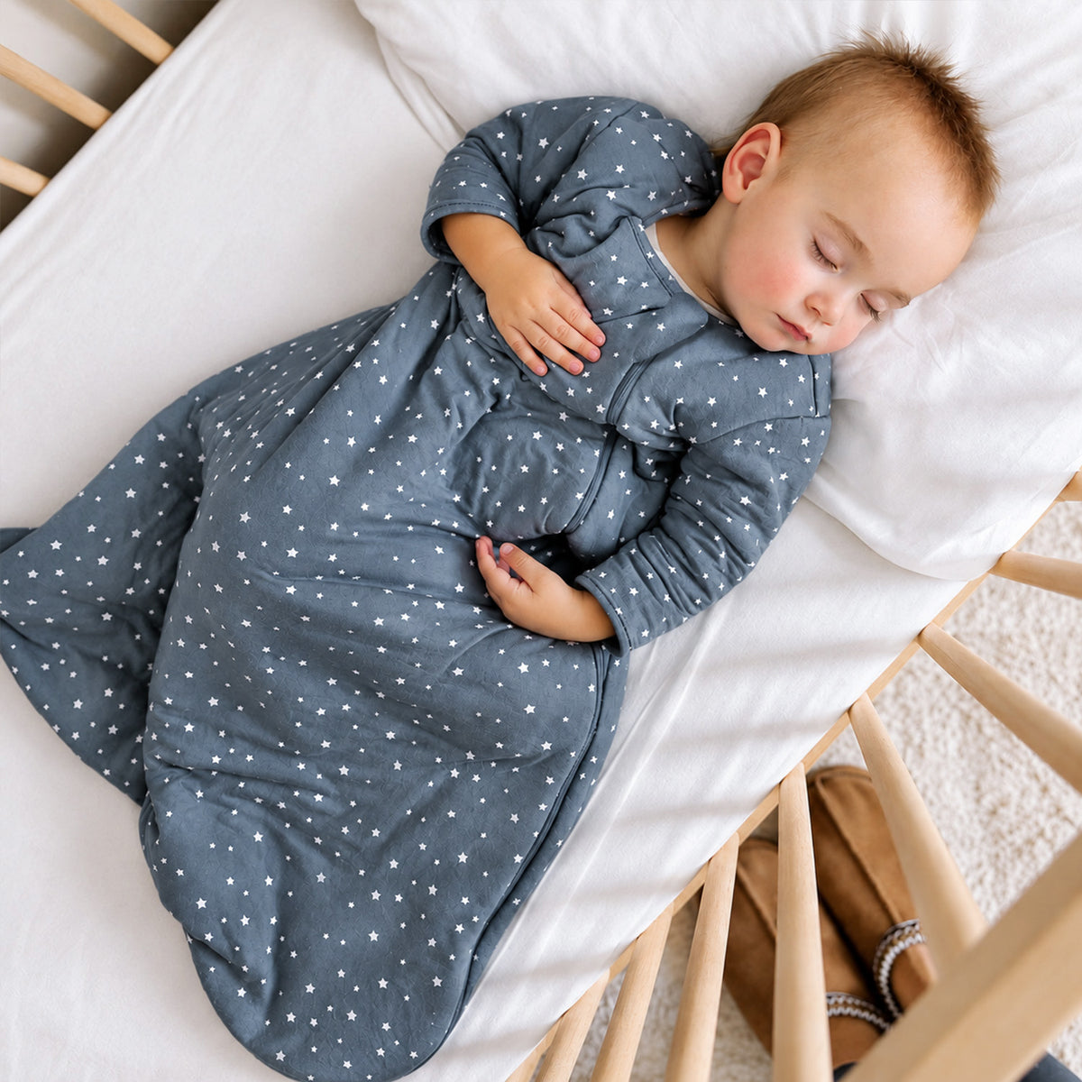 Baby wearing a slate blue star-print sleep sack with long sleeves and a covered foot area.