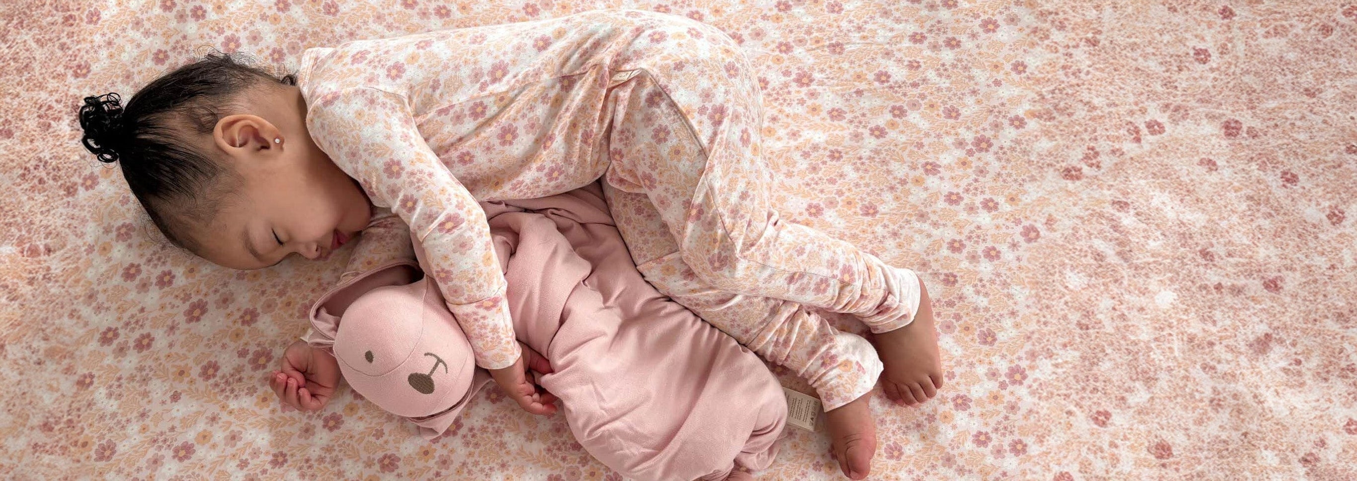 Child sleeping on a floral bedspread with a pink plush toy