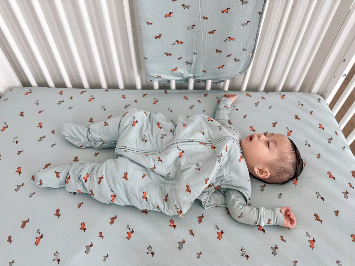 Light blue crib sheet with orange dog print pattern, baby lying on back