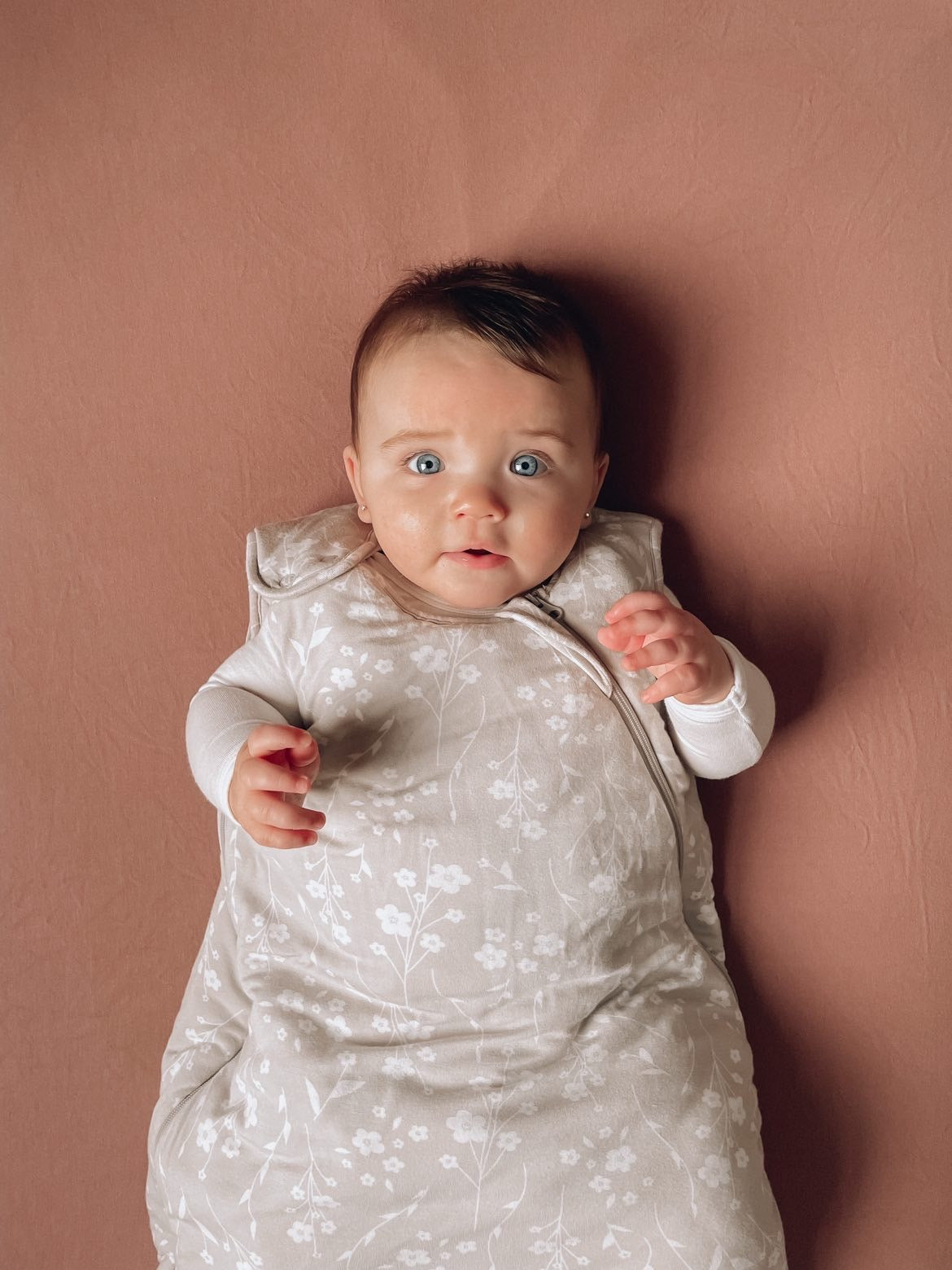 baby girl on a pink sheet with a floral printed bamboo sleep bag, photographed from above