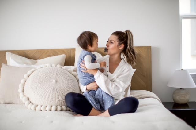 mother holding her son wearing a gunamuna sleep sack on a white bed