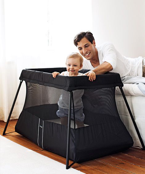 smiling baby in a black travel playpen with his father smiling behind him