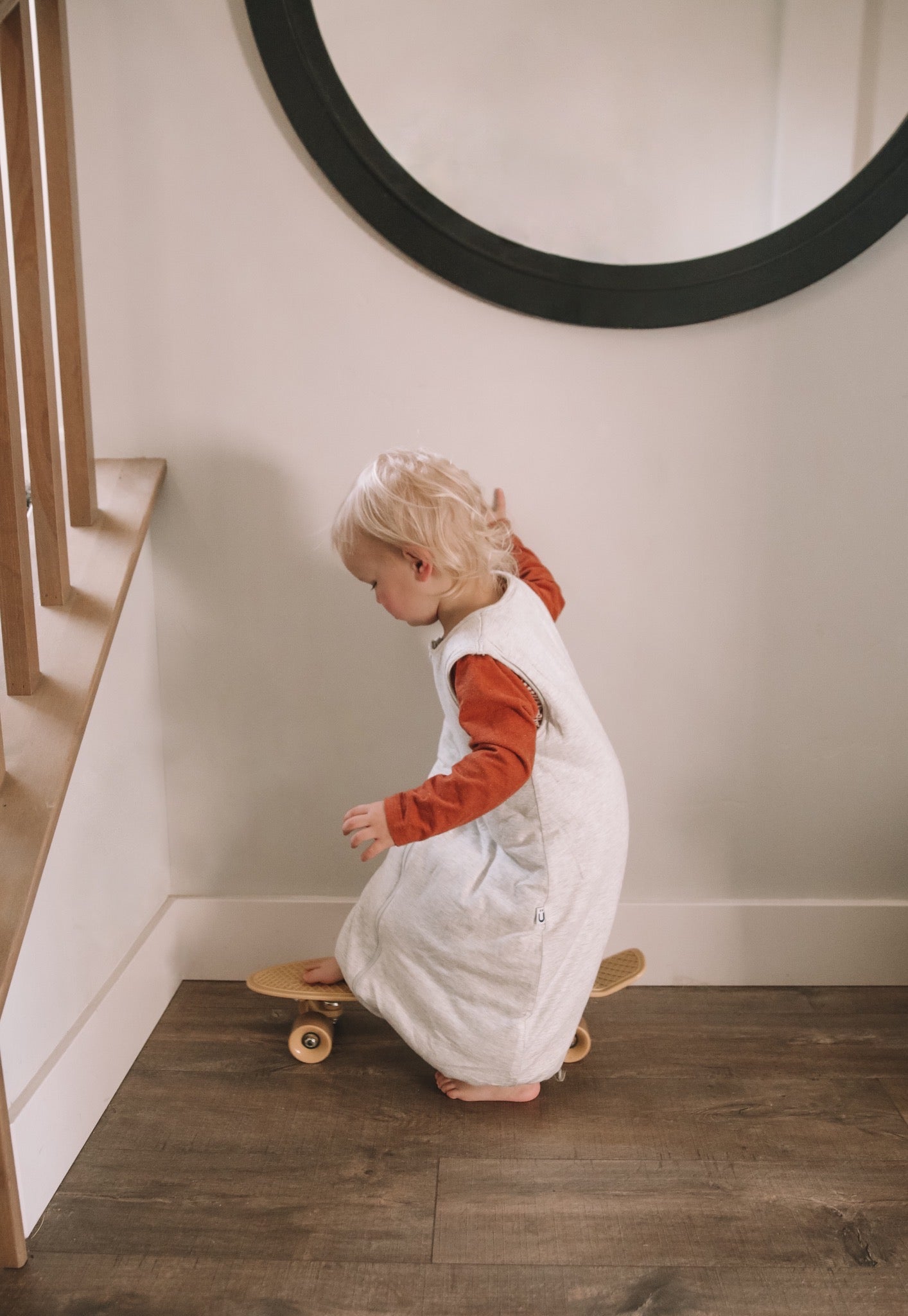 toddler in a white gunamuna sleep bag, playing inside the house on a skateboard