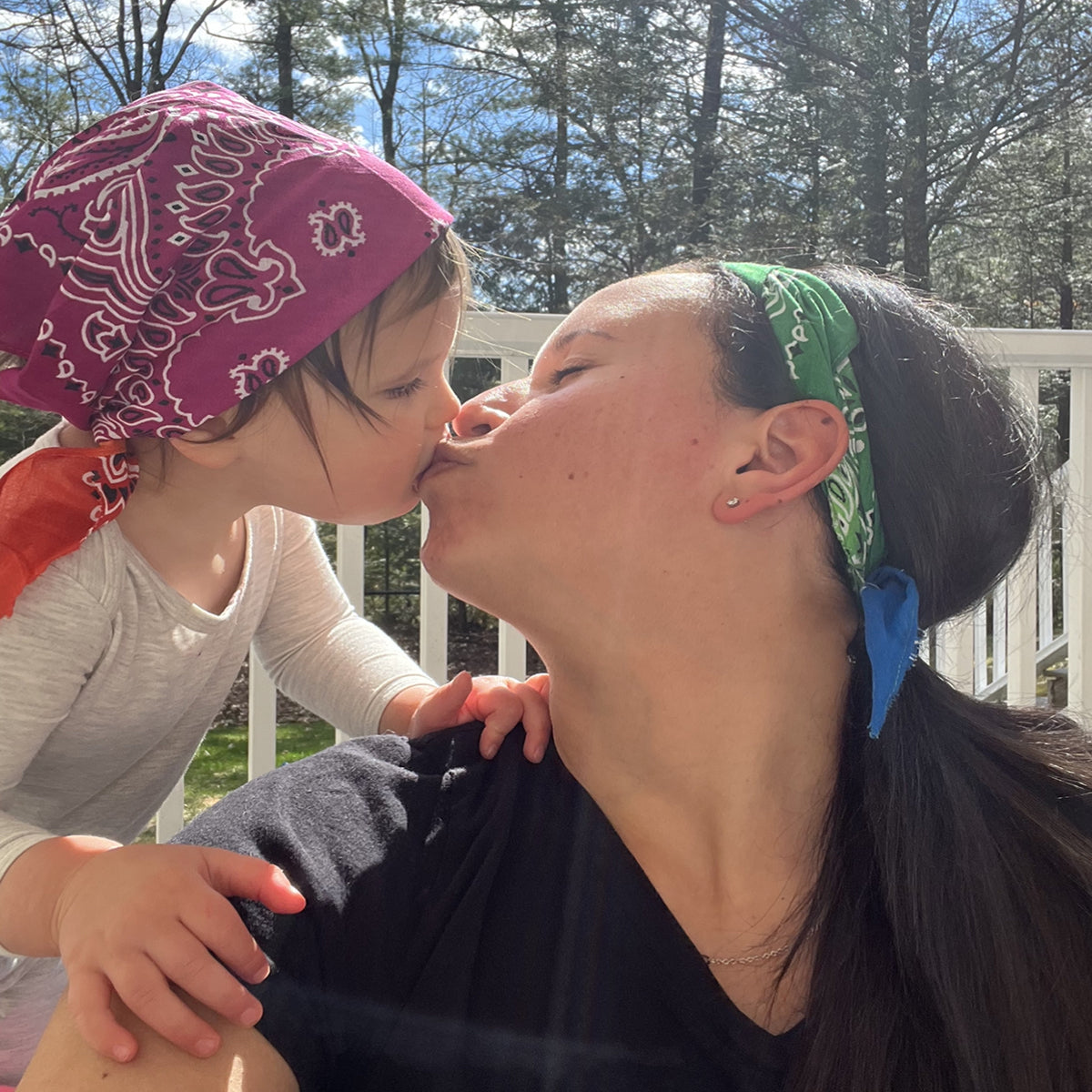 momma giving her daughter a kiss, both are wearing bandanas