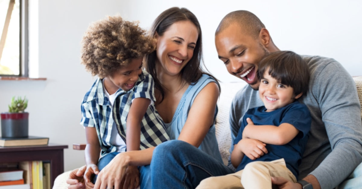 multicultural family: mom, dad, and two boys laughing and smiling on a couch