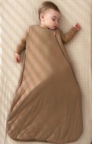 baby asleep on a beige bed wearing sustainable bamboo convertible footie pajamas and bamboo sleep bag set in brown neutral tones. bag is unzipped for easy diaper change