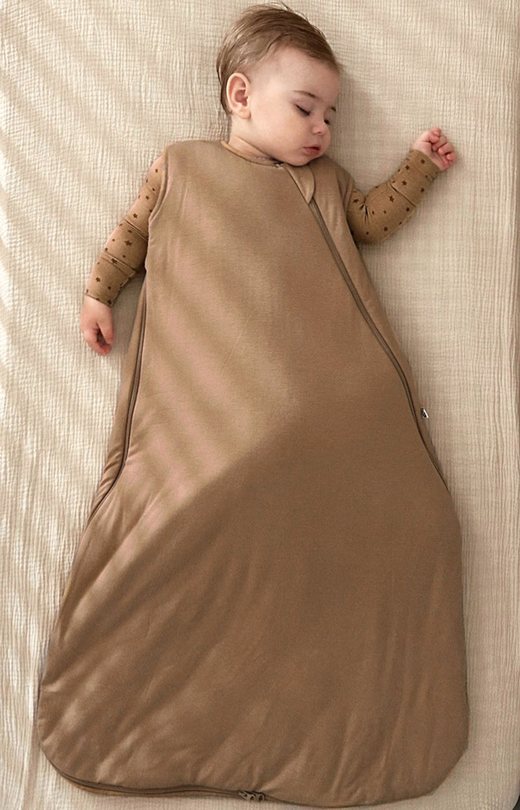 baby on a beige bed zipped up in sustainable bamboo convertible footie pajamas and bamboo sleep bag set in brown neutral tones