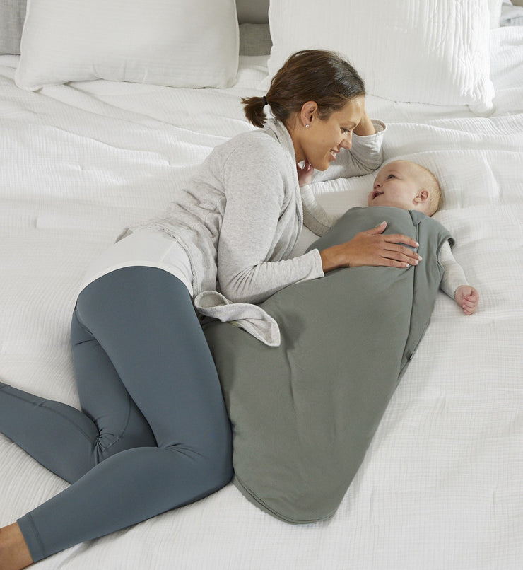 mother cuddling baby on a white bed. baby is wearing sustainable bamboo convertible footie pajamas and bamboo sleep bag set in sage