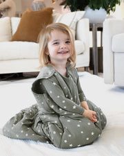 toddler sitting on floor wearing sustainable bamboo convertible footie pajamas and bamboo sleep bag set in forest green with white printed stars