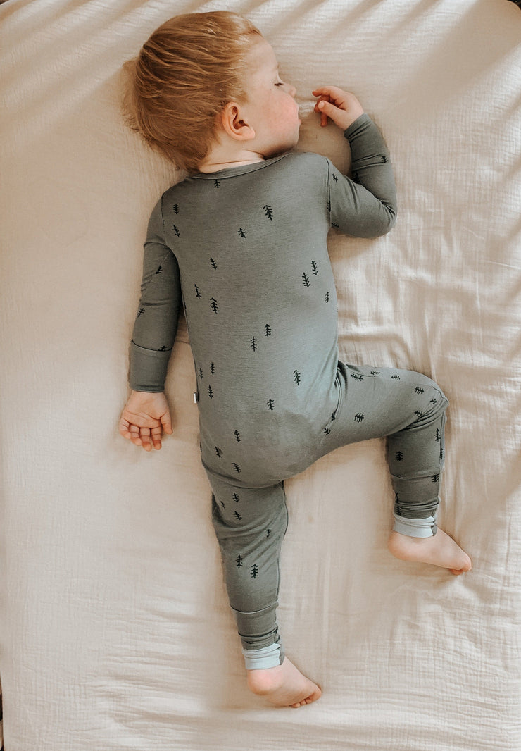 toddler on bed asleep on stomach wearing sustainable bamboo convertible footie pajamas set in forest green with dark green printed trees