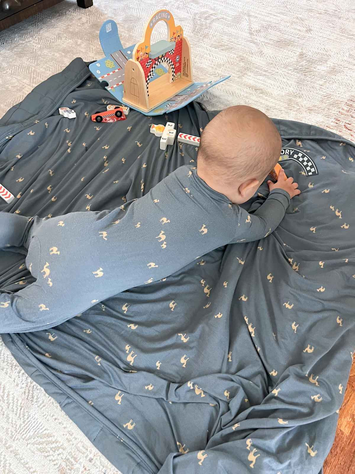 Dark blue camel-pattern play blanket draped with activity book panel and patch