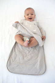 smiling baby with unzipped neutral goose printed sleep sack during a diaper change