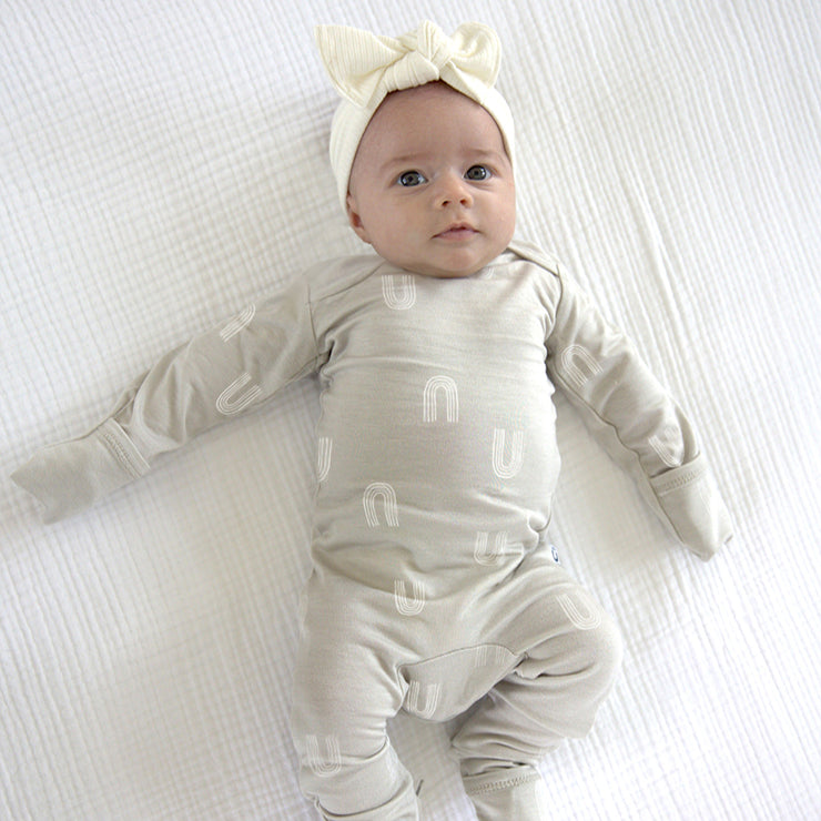 baby girl on white sheets with sustainable bamboo convertible footie pajamas in neutral rainbow print for rainbow babies