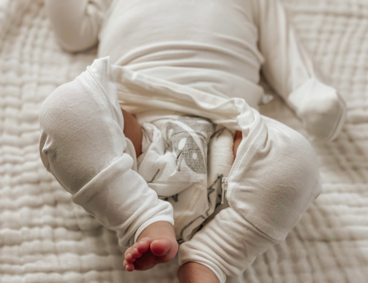 baby on a white sheet wearing undyed hypoallergenic baby pajamas for sensitive skin. up close shot of the diaper zipper during a diaper change