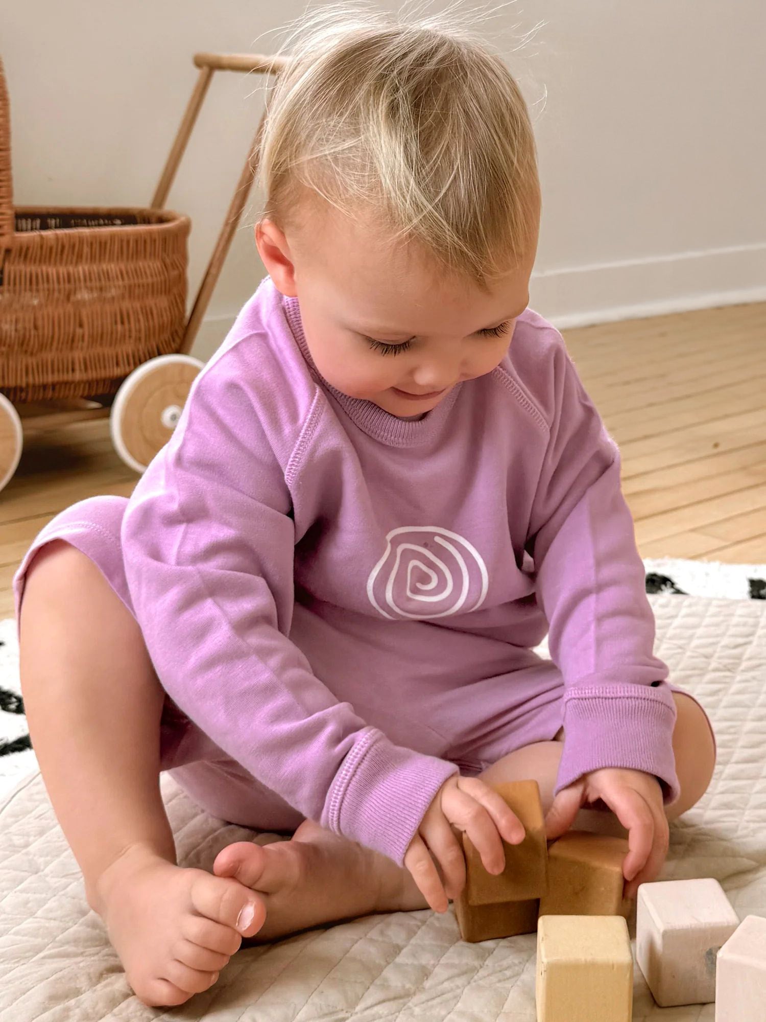 Lilac crewneck sweatshirt with white lollipop swirl logo, sitting pose