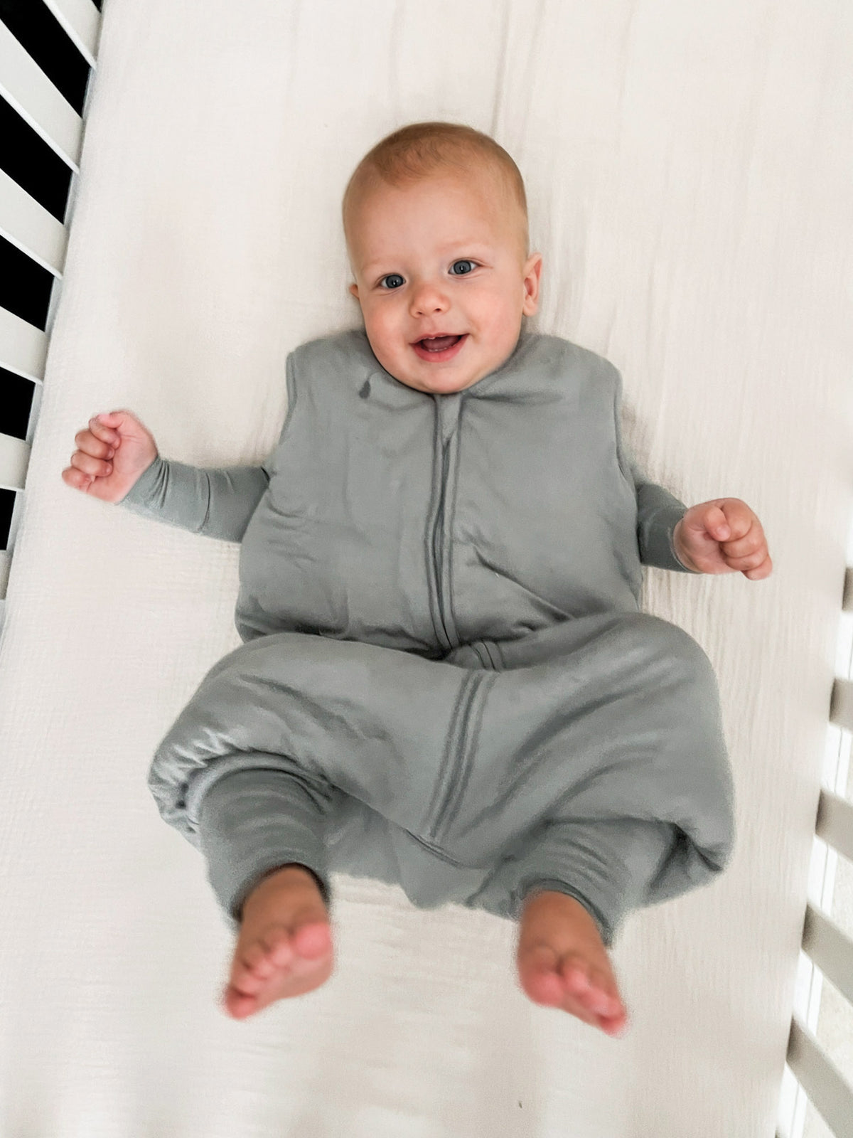 Sage green zip-front footie sleep sack with long legs and sleeves on standing baby