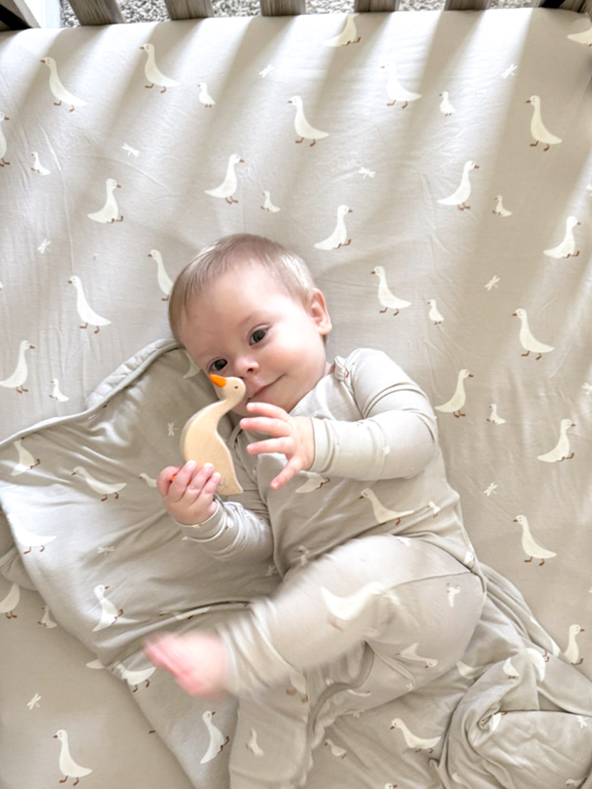 Goose-pattern crib sheet with scattered white geese on light cream background