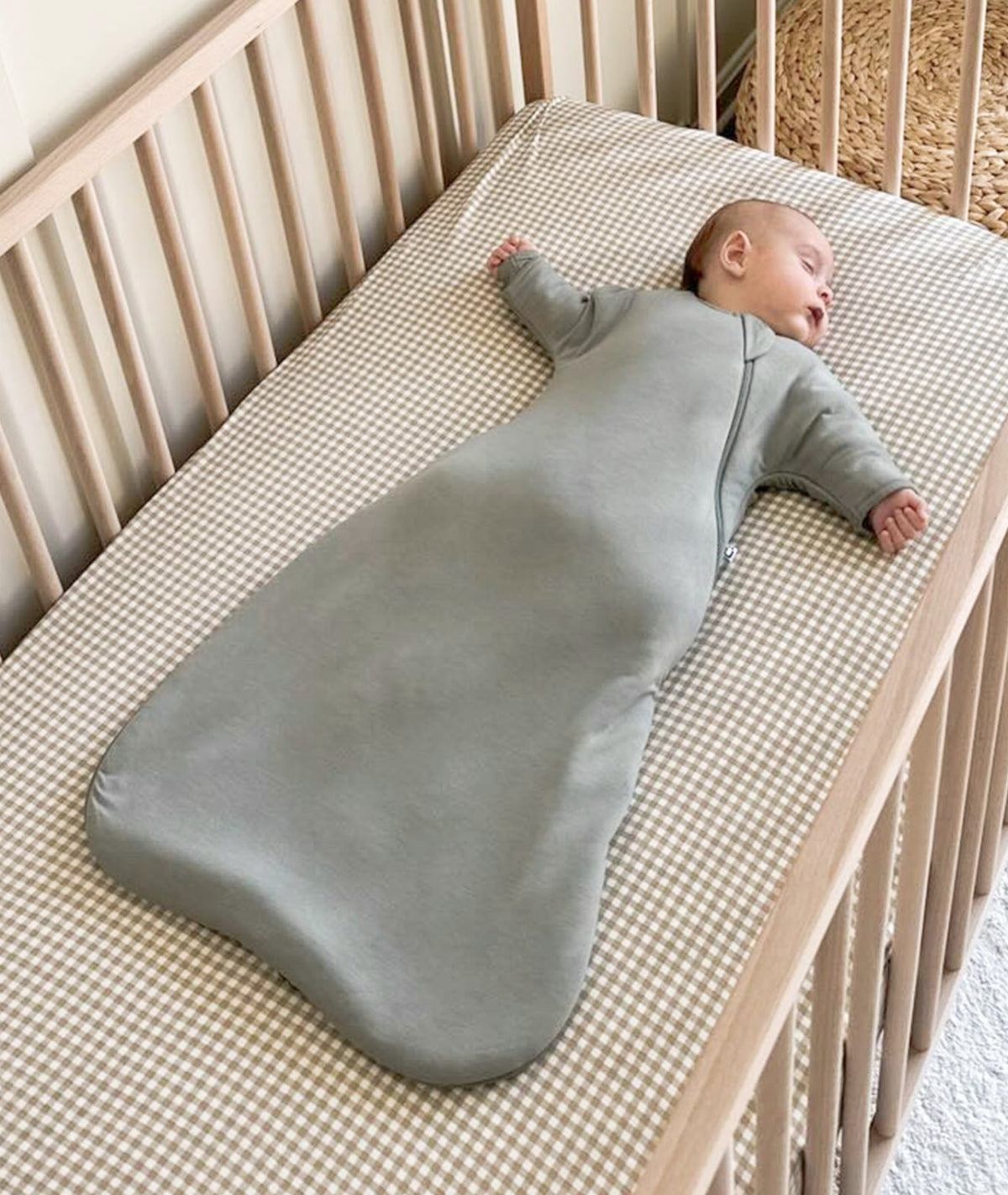 Sage green swaddle sack laid flat with long sleeves and front zipper opening