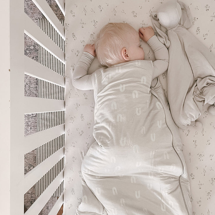 baby sleeping belly down in all white crib with sustainable bamboo sleep sack in neutral rainbow print for rainbow babies