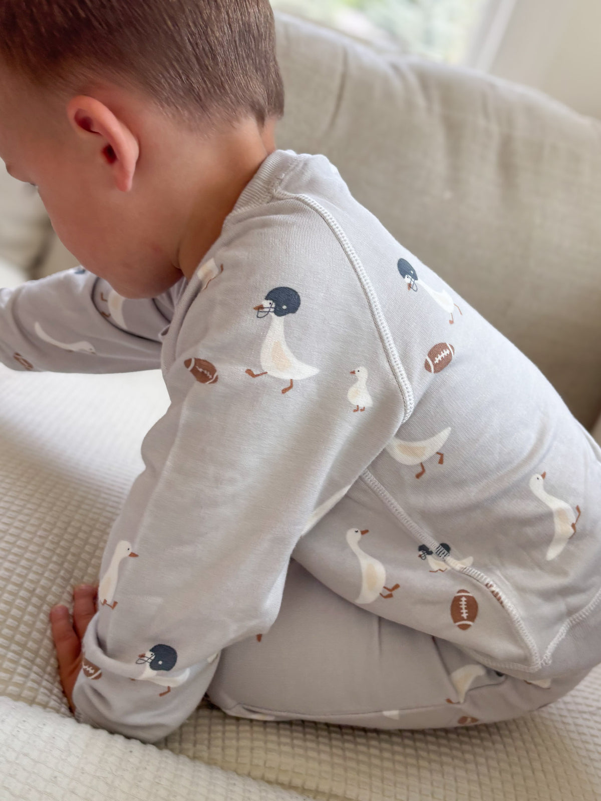 Kids fleece sweatsuit with duck and football print, toddler crawling on a sofa