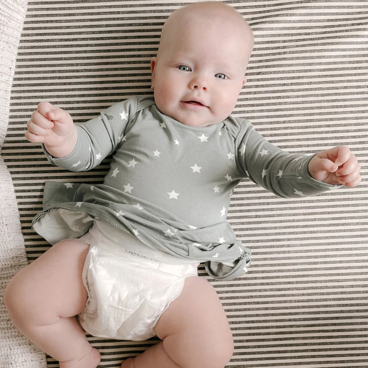 Sage green baby romper with long sleeves and white star print, lying pose