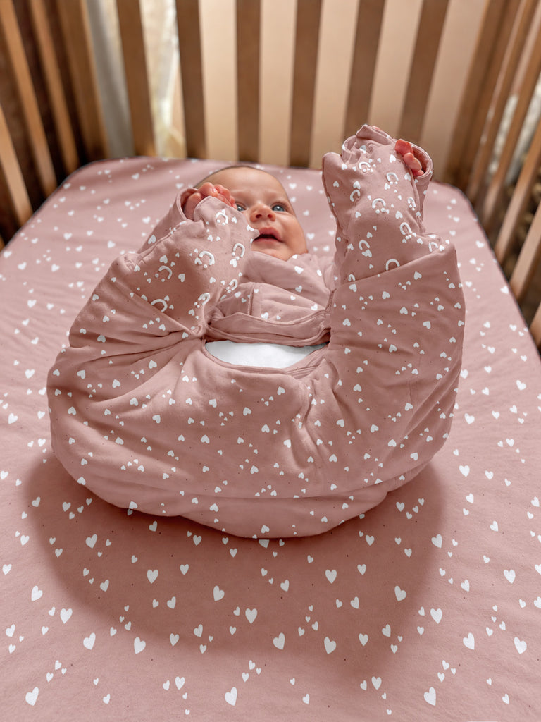 Pink heart-patterned footie sleep sack, folded, with long sleeves and enclosed feet