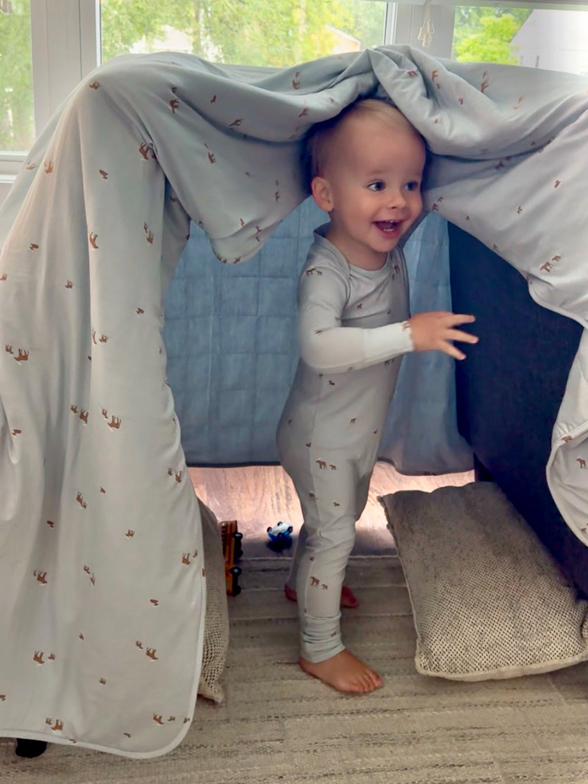 Light gray baby blanket with moose print, draped like a play tent around a smiling toddler.