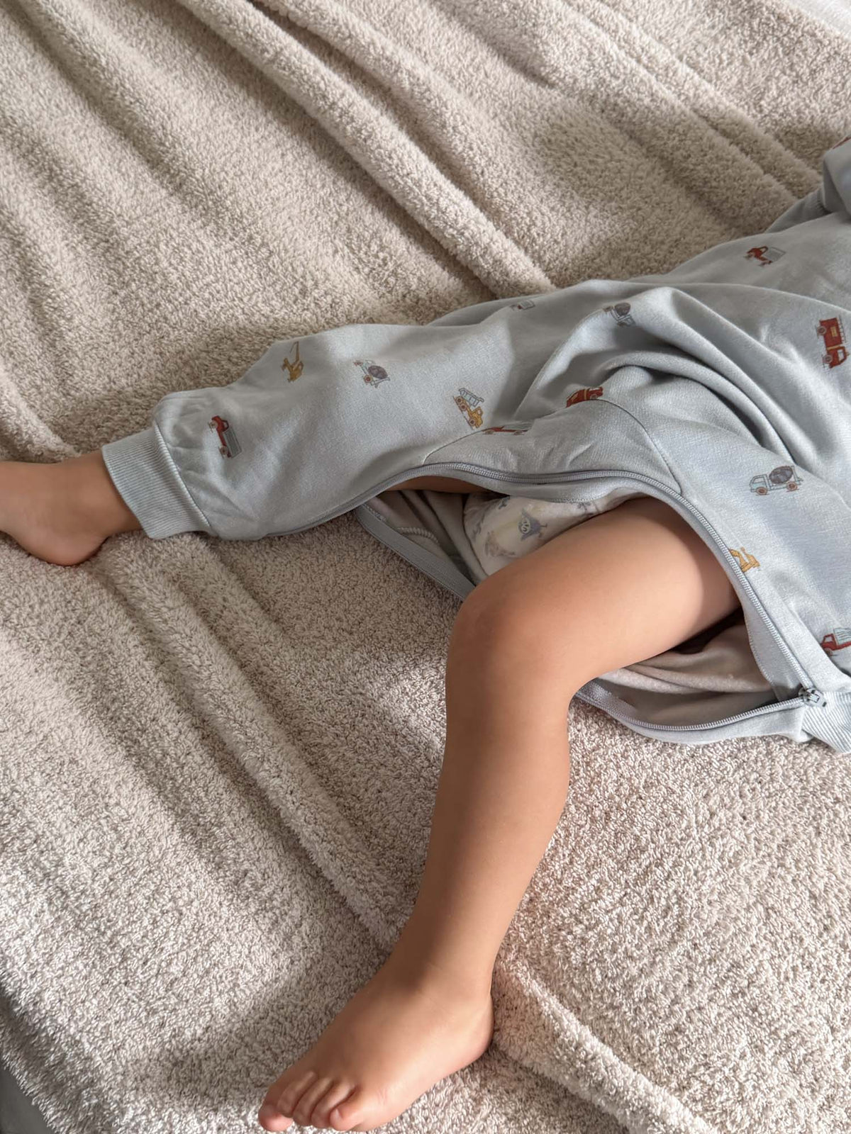 Fleece baby jumpsuit in light gray with colorful vehicle print, lying down side view