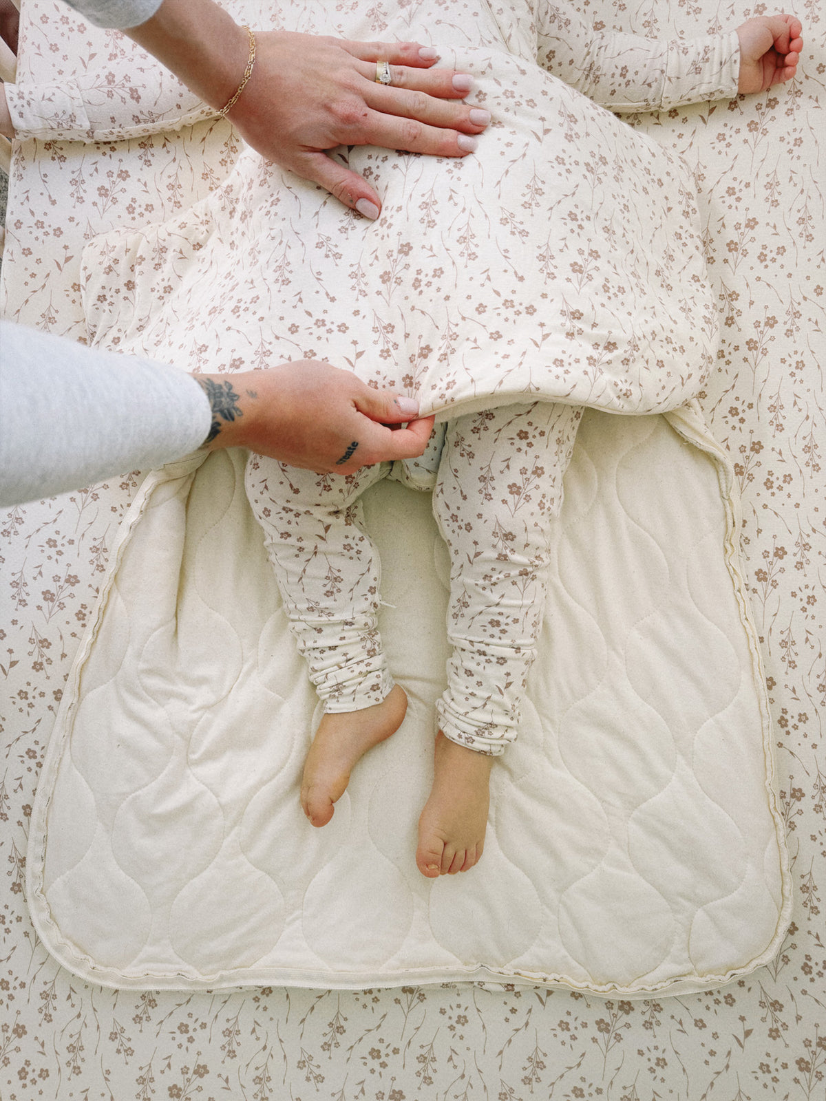 Cream floral long-sleeve sleep sack with open bottom flap, caregiver adjusting